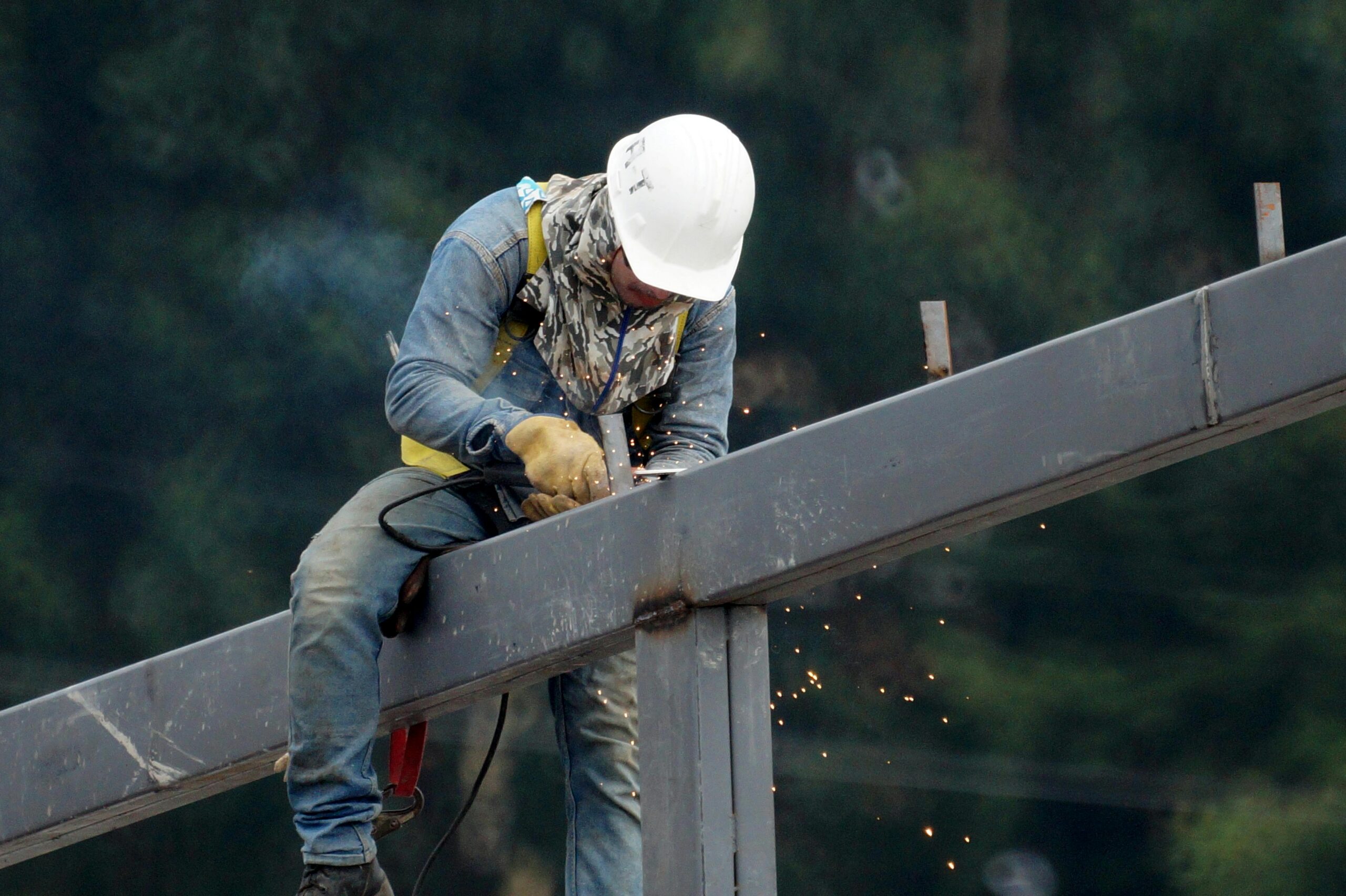 A construction worker welds a steel beam with sparks flying, showcasing industrial work.