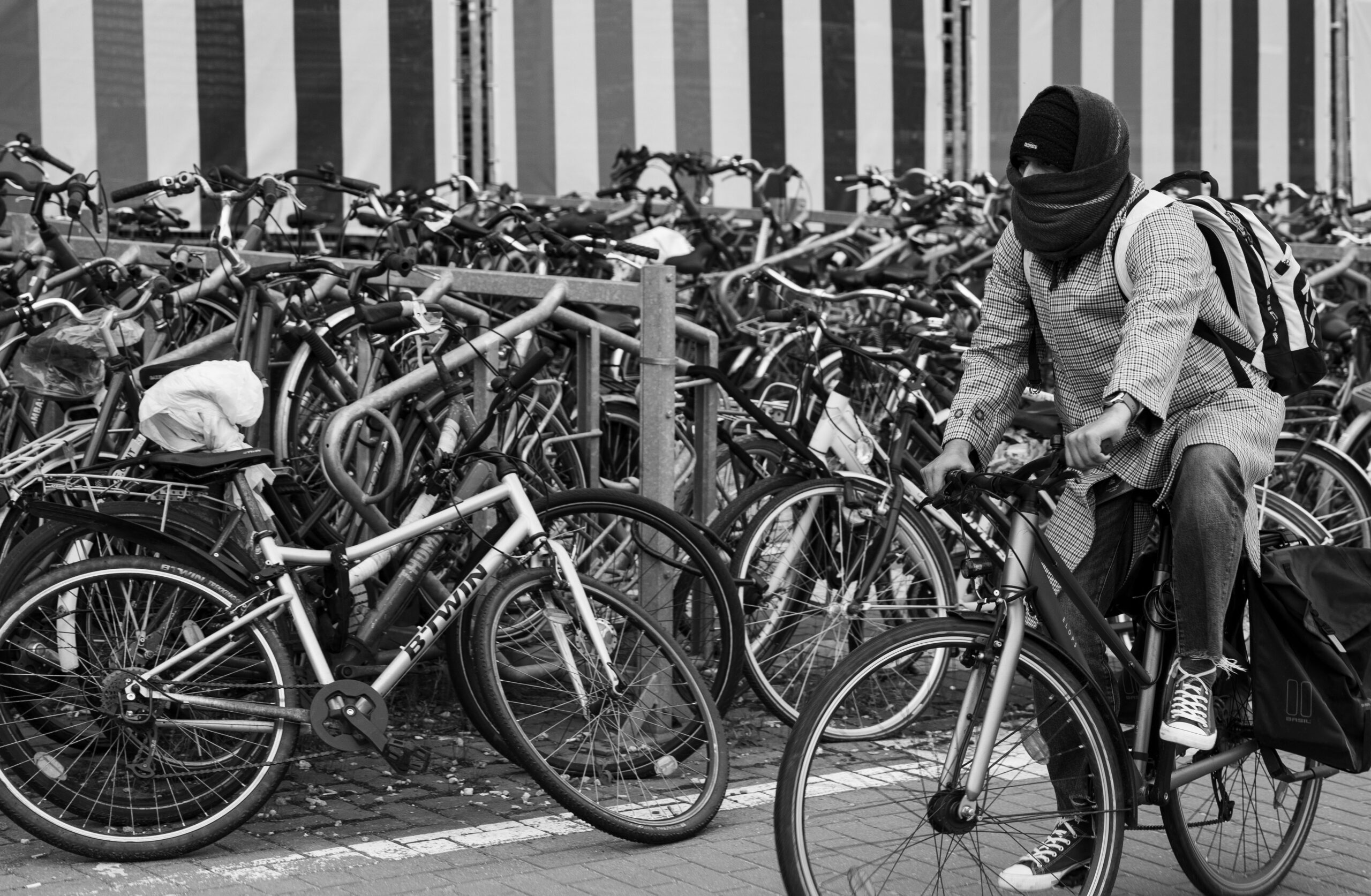 Black and white photo of a cyclist navigating a crowded bicycle parking area.