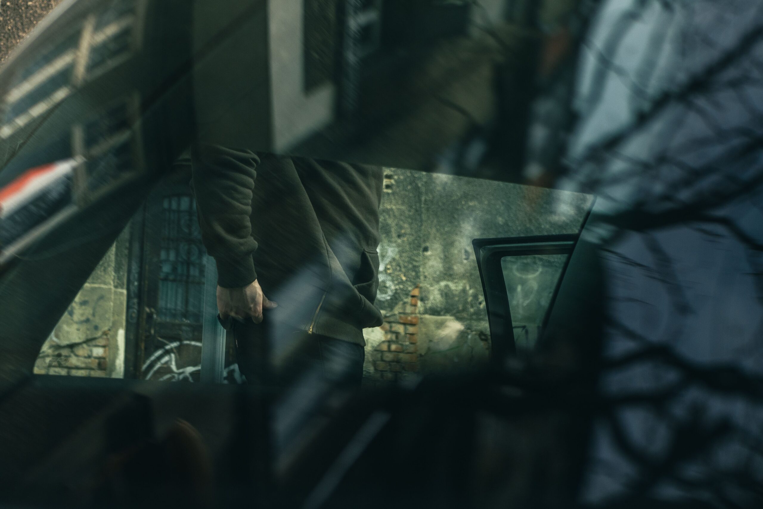 Reflection of a person in car window in an urban environment, capturing a moody industrial vibe.