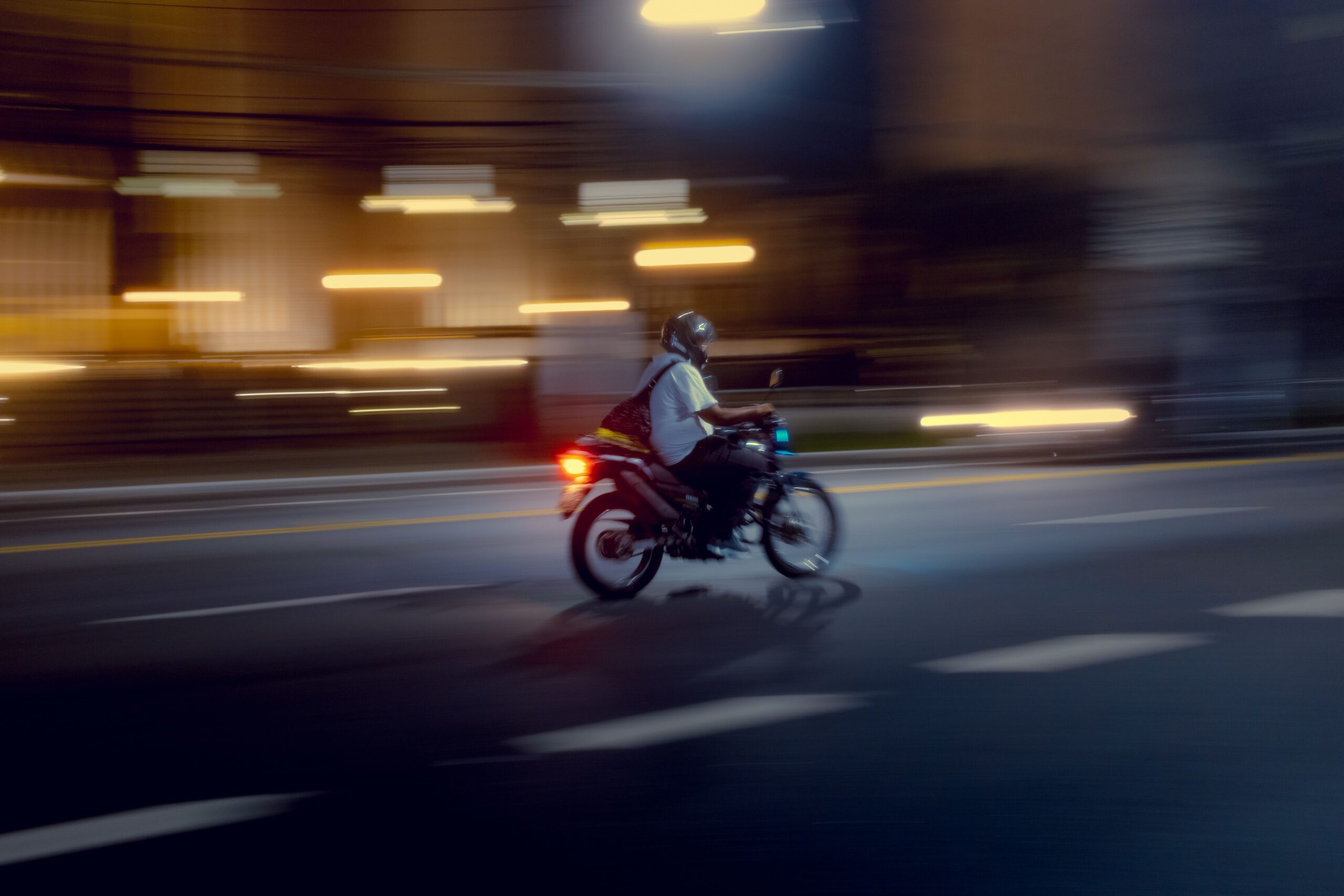 A motorcyclist rides through a blurred city street at night, capturing motion and vibrant lights.