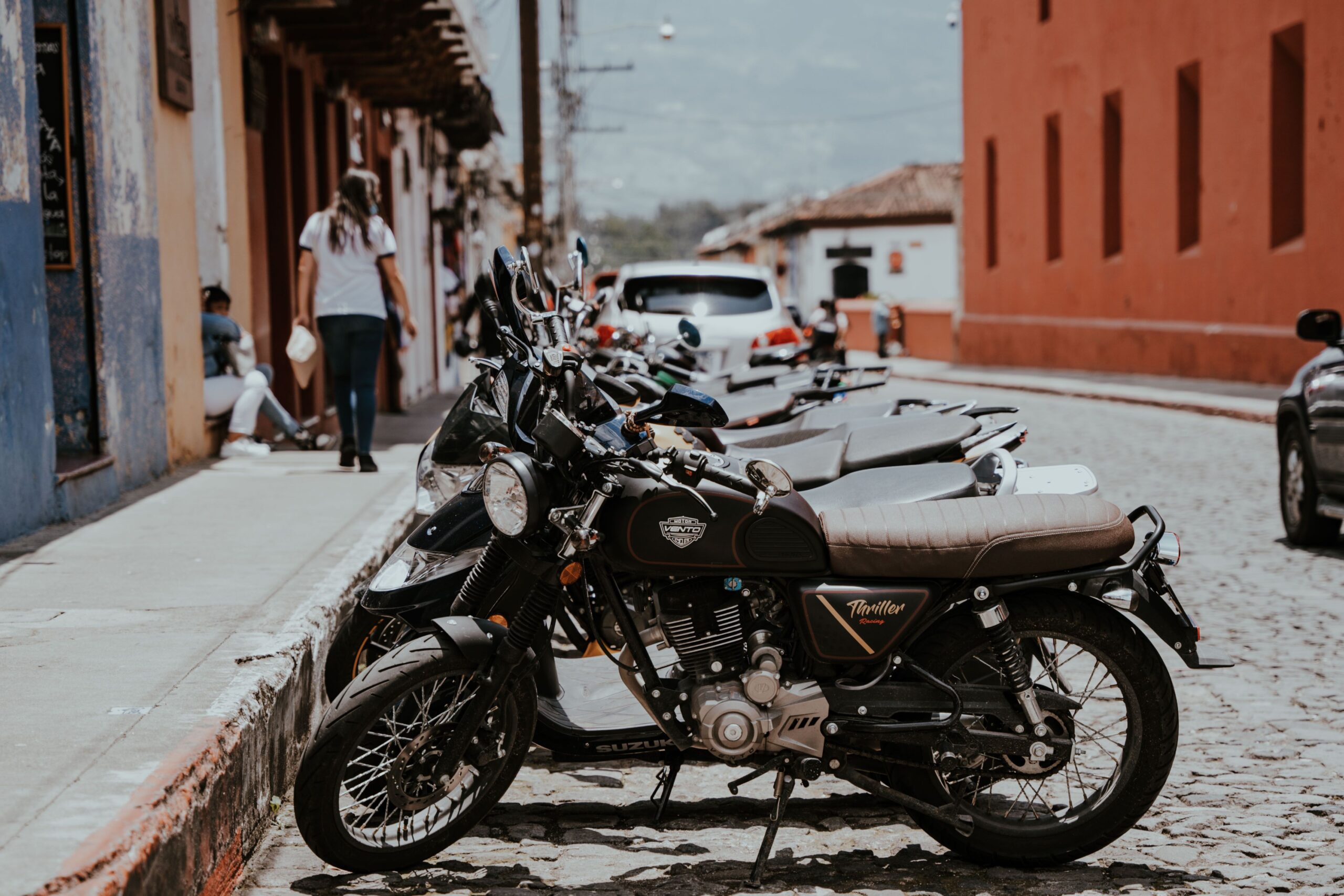 A row of parked motorbikes along a cobblestone street in an urban setting.