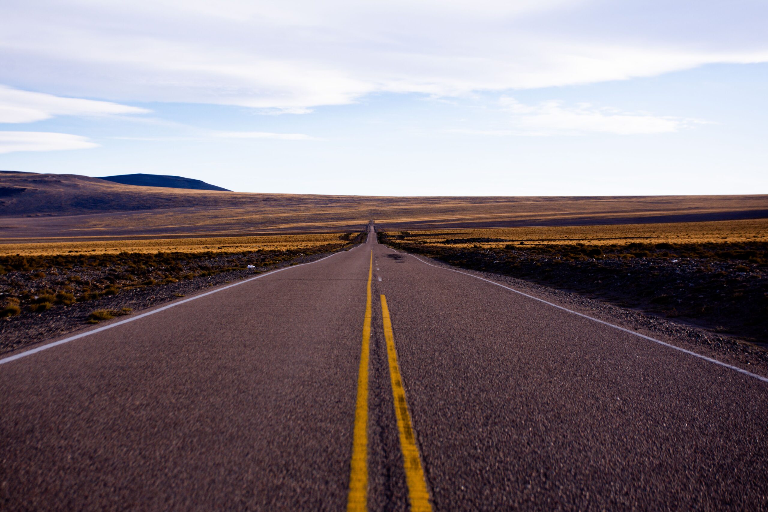A wide shot of an empty road stretching through a barren desert under a clear sky.